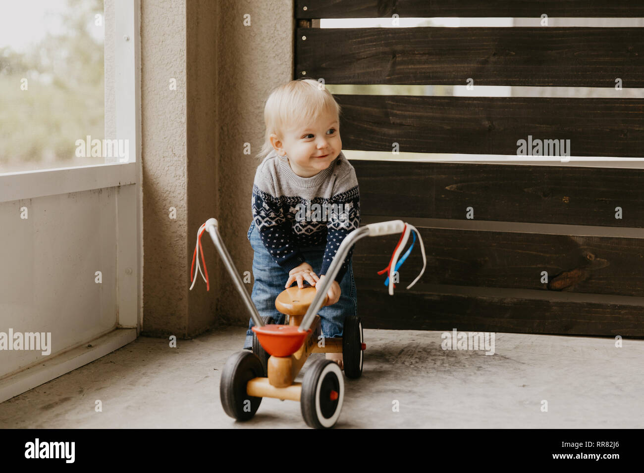 Kostbare adorable kleine süße blonde Baby Kleinkind Junge Spielen draussen auf Holzspielzeug Fahrrad Roller Mobile lächelt in die Kamera und Spaß Stockfoto