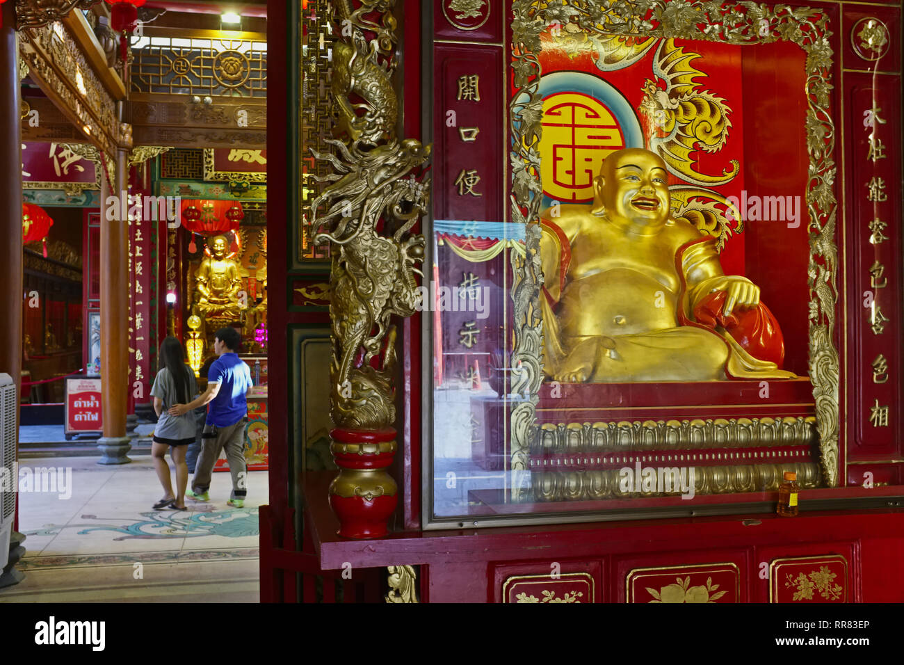 In taoistischen Tempel Wat Mangkon Kamalawat, Chinatown, Bangkok, Thailand, ein junges Paar übergibt die wichtigsten Heiligtum; Rechts: ein hotei oder Lachender Buddha Stockfoto