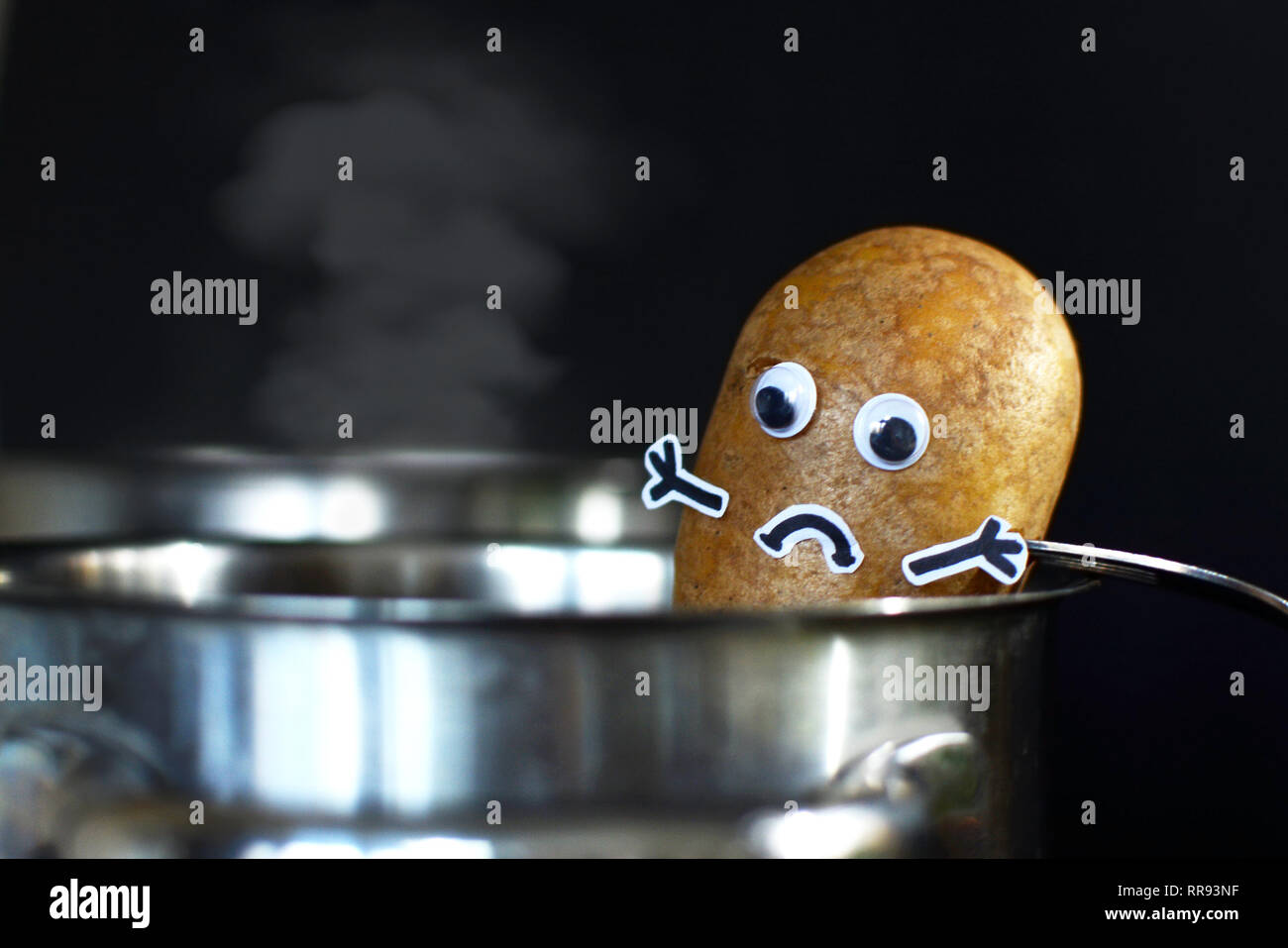 Kartoffel mit einem traurigen Gesicht in einem dampfenden Kochtopf auf dunklen schwarzen Hintergrund gesetzt werden Stockfoto