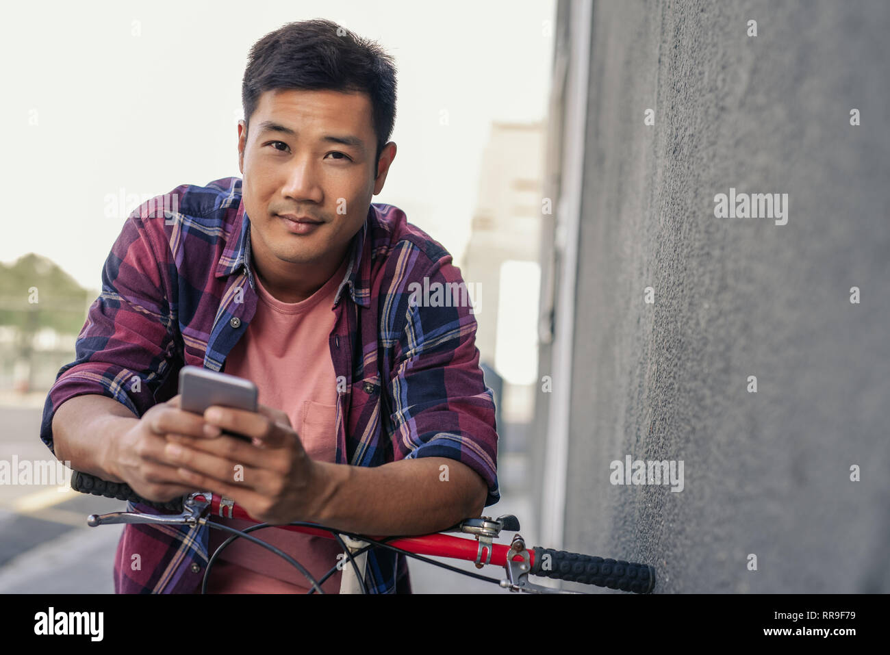 Lächelnden jungen Mann über sein Fahrrad einen Text zu lesen Schiefe Stockfoto