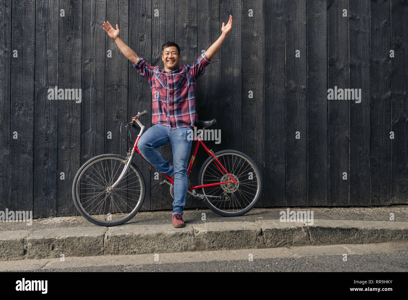 Lächelnden jungen Mann mit einem Fahrrad seine Arme gen Himmel heben Stockfoto