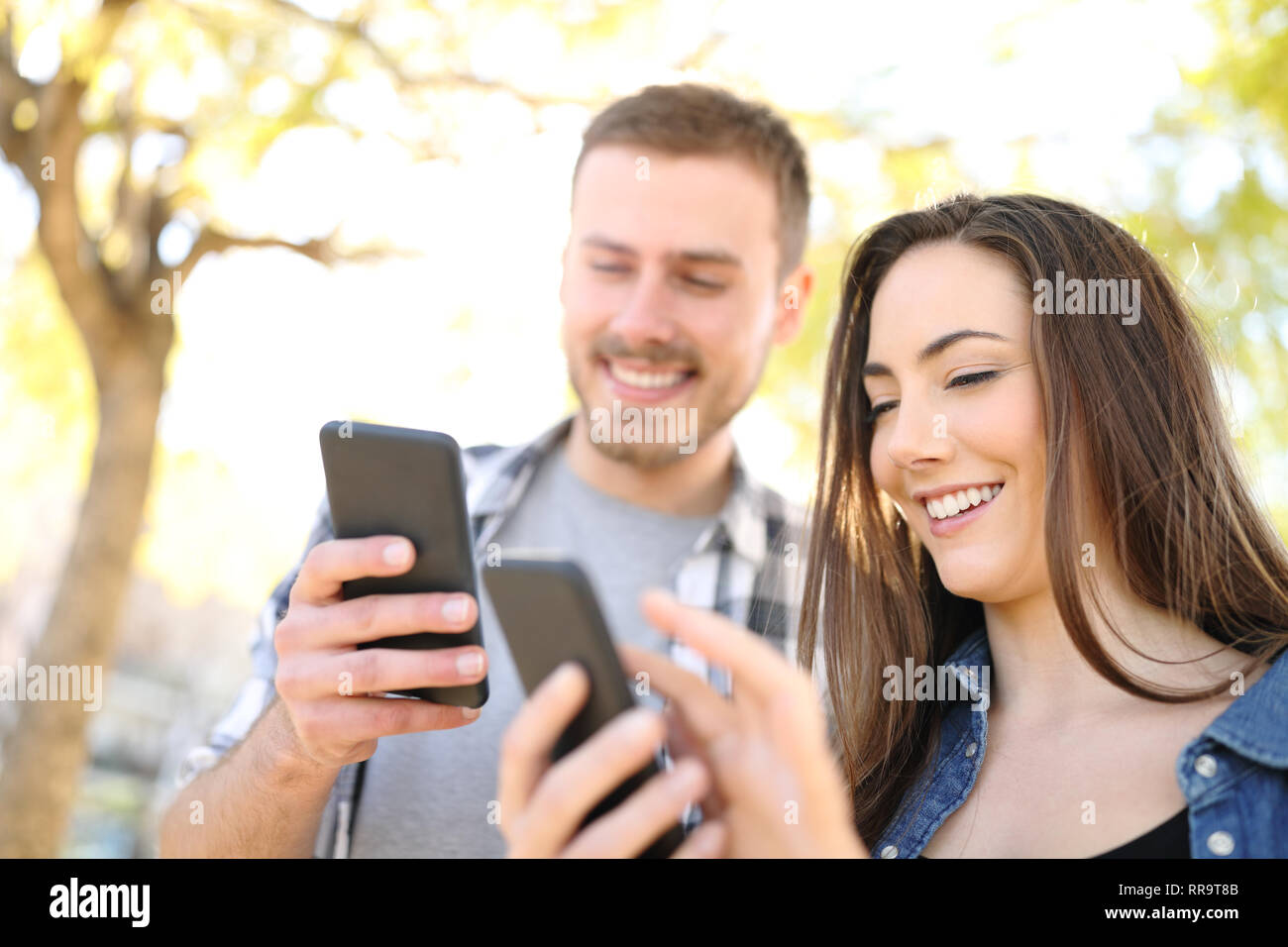Zwei glückliche Freunde über ihre Smartphones stehen im Freien in einem Park Stockfoto
