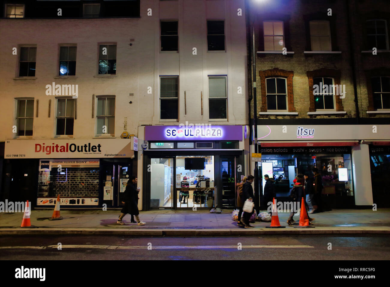 Menschen zu Fuß vorbei an Geschäften in der Nacht der Tottenham Court Road, London, England, Großbritannien Stockfoto