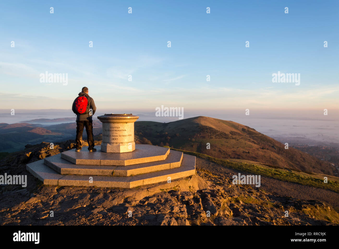 Ein einsamer Wanderer auf dem Gipfel des Worcestershire Beacon, Malvern Hills, Worcestershire, an einem nebligen Winter sunsrise. UK. Stockfoto