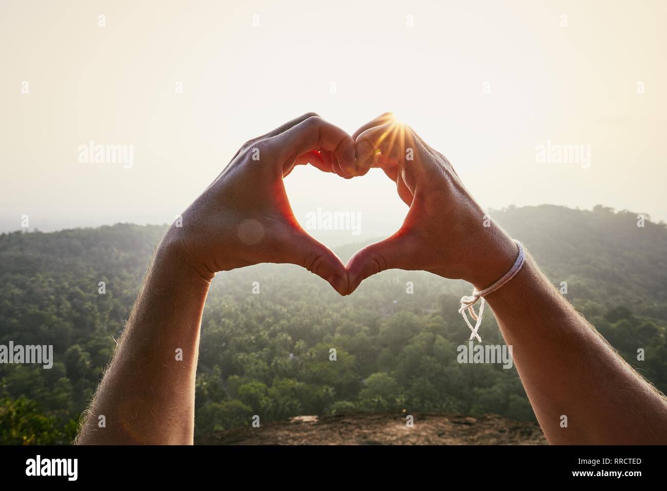 Nahaufnahme der Hände und Herzen Form gegen die Landschaft bei Sonnenuntergang. Stockfoto