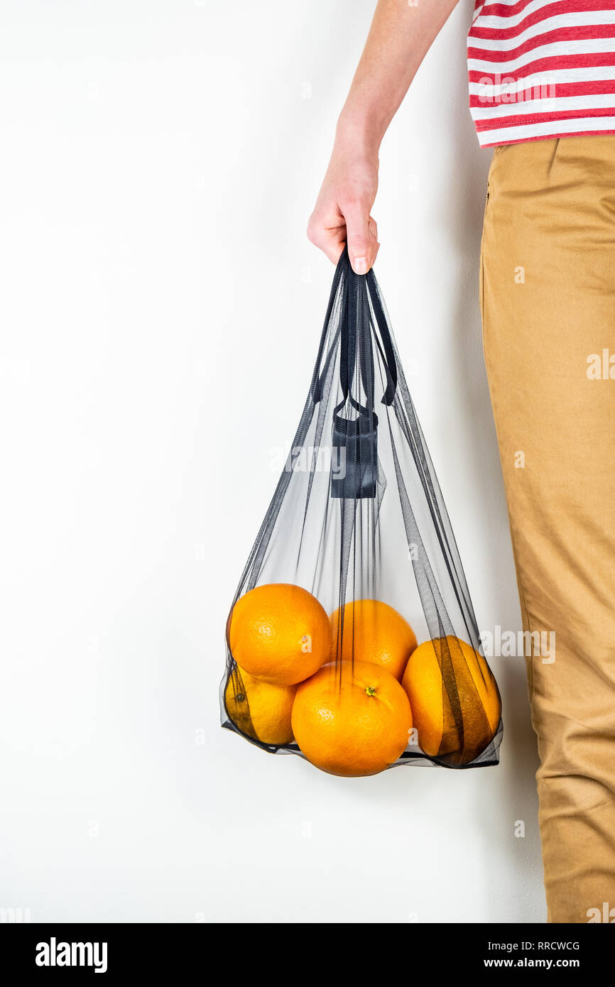 Holding eine wiederverwendbare string Beutel voll von Orangen. Nachhaltige ökologische Verpackungskonzept: Einkaufsmöglichkeiten für Lebensmittel mit einem Multi-bag Ökologische foo zu verringern Stockfoto