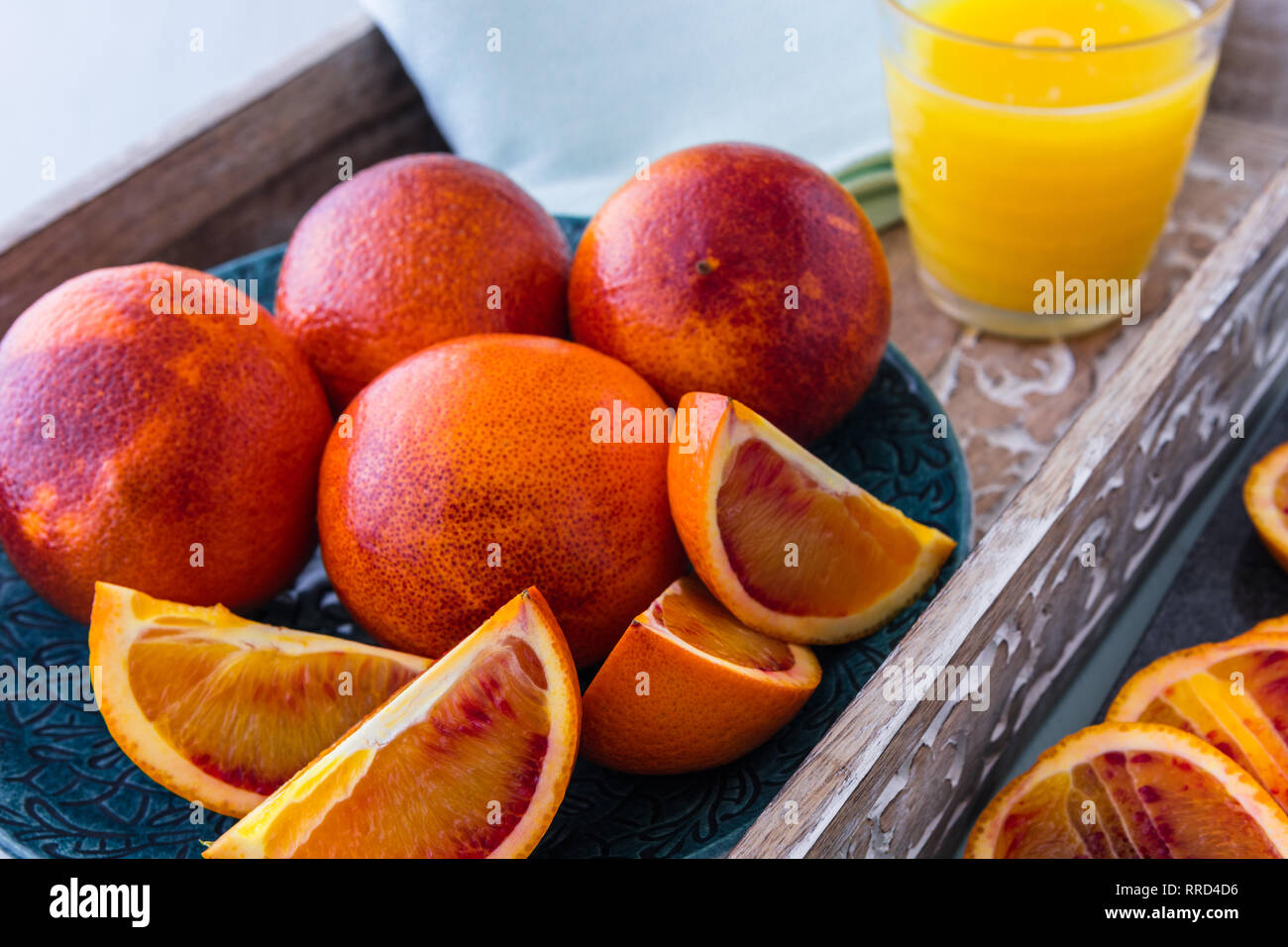 Blutorangen Ganze und Aufgeschnittene auf Platte und Fach mit einem Glas Orangensaft im Hintergrund Stockfoto
