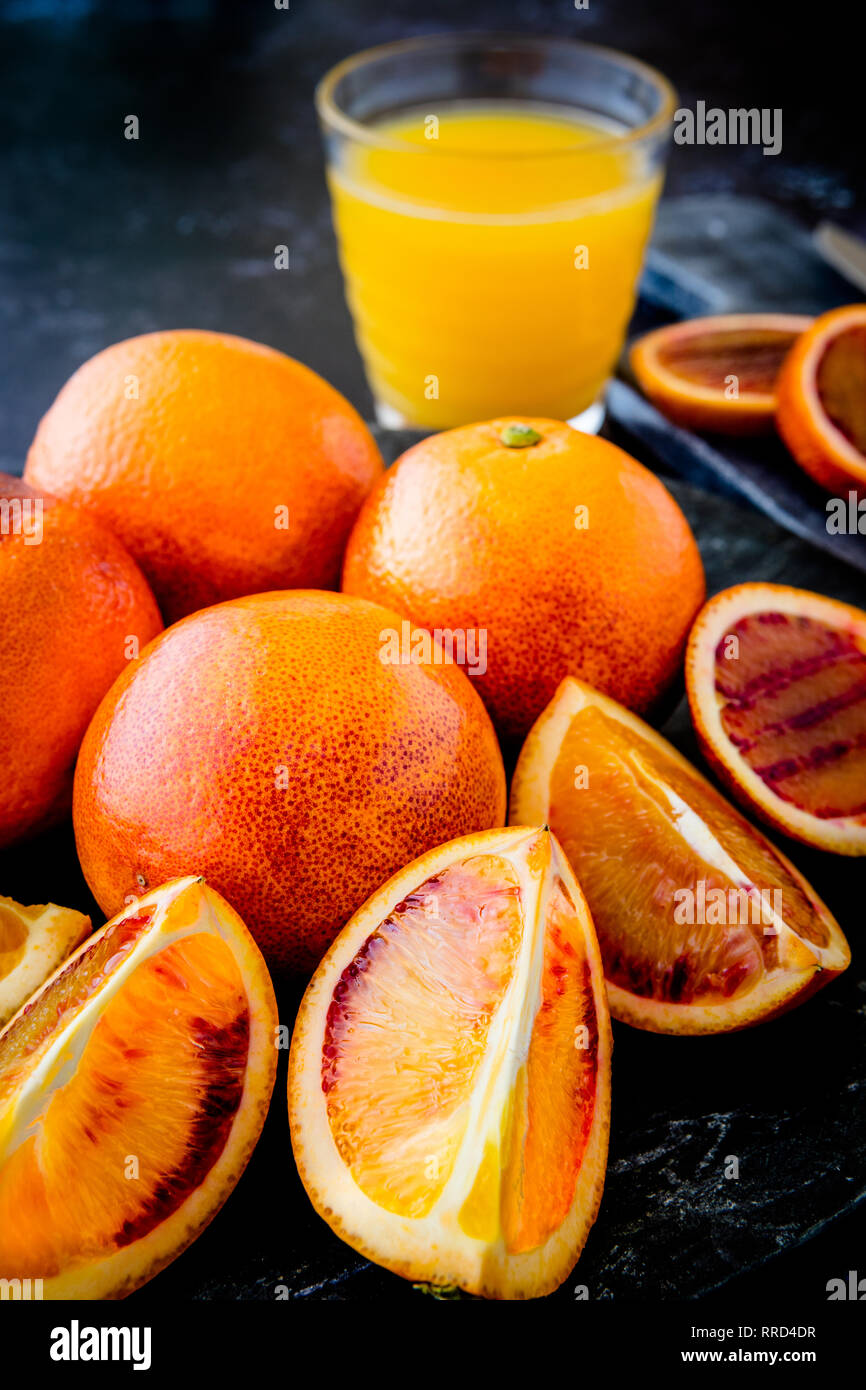 Frischen saftigen Blutorangen Ganze und Aufgeschnittene auf dunklen Platte mit Glas Orangensaft und Schichten im Hintergrund - geringe Tiefenschärfe Stockfoto
