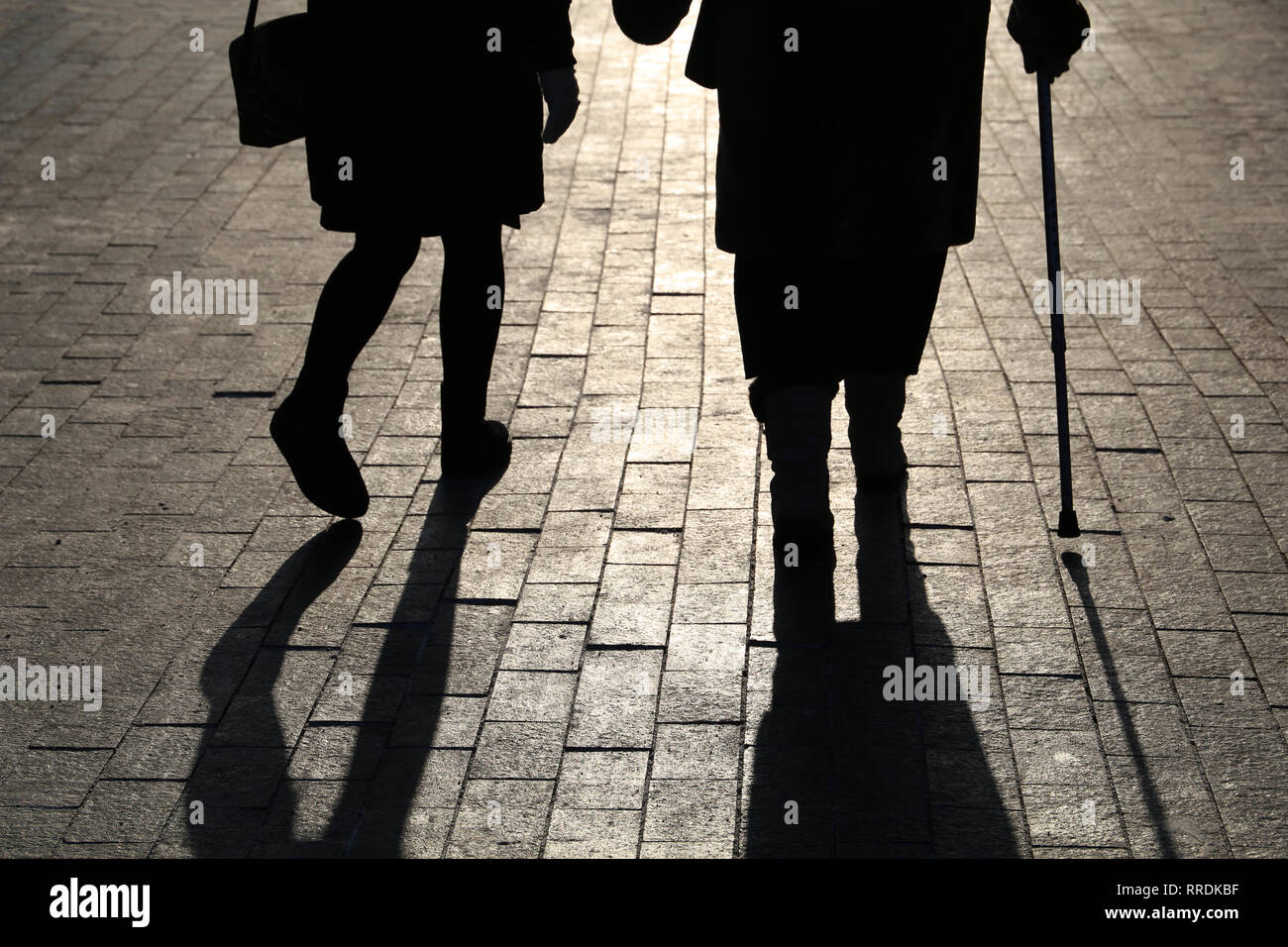 Mädchen und Frau mit einem Stock, schwarze Silhouetten und Schatten von zwei Menschen zu Fuß auf der Straße. Konzept der hinkend, Alter, ältere oder blinde Person Stockfoto