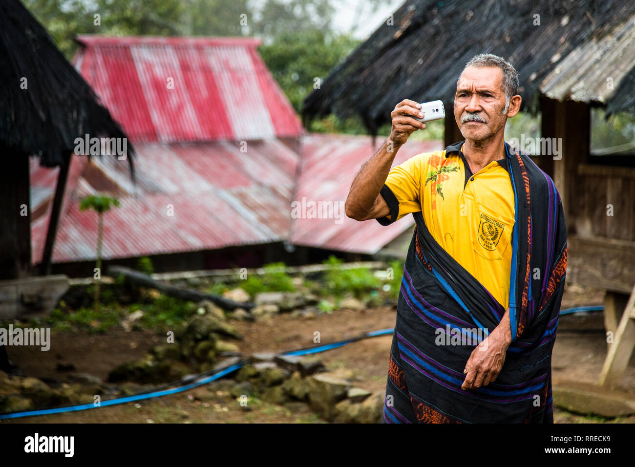 Indonesischer Mann im traditionellen Outfit über t-shirt Fotografieren mit Handy Stockfoto