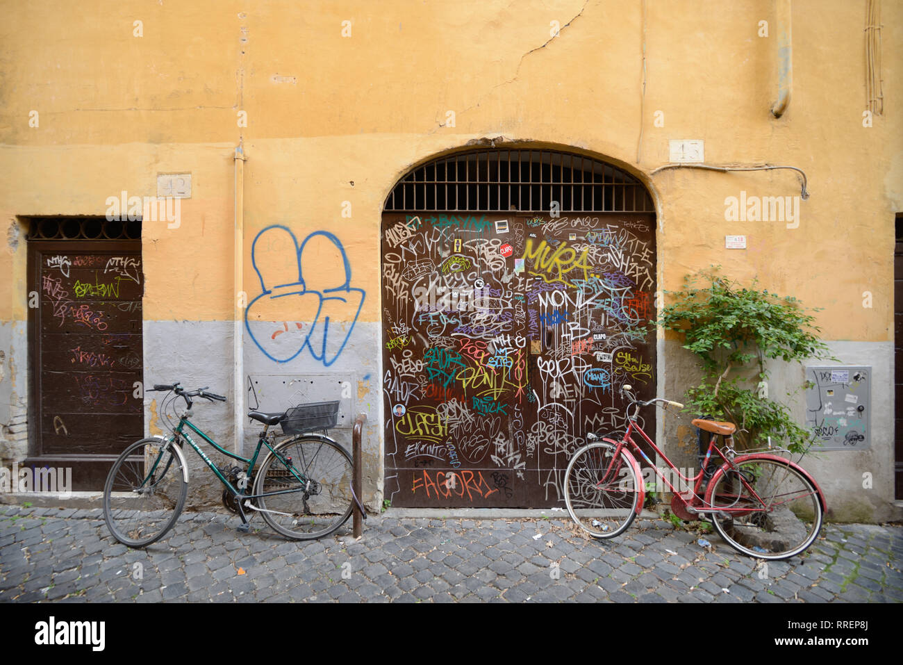 Street Scene mit Abgestellte Fahrräder und Graffiti bedeckt ockerfarbenen Wände im eleganten und historischen Viertel Trastevere, Rom, Italien Stockfoto