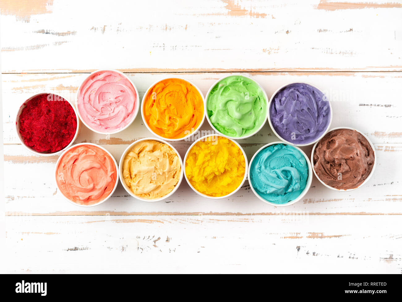 Viele Tassen mit bunten Regenbogen Eis auf weißem Holz- Hintergrund. Ansicht von oben Stockfoto