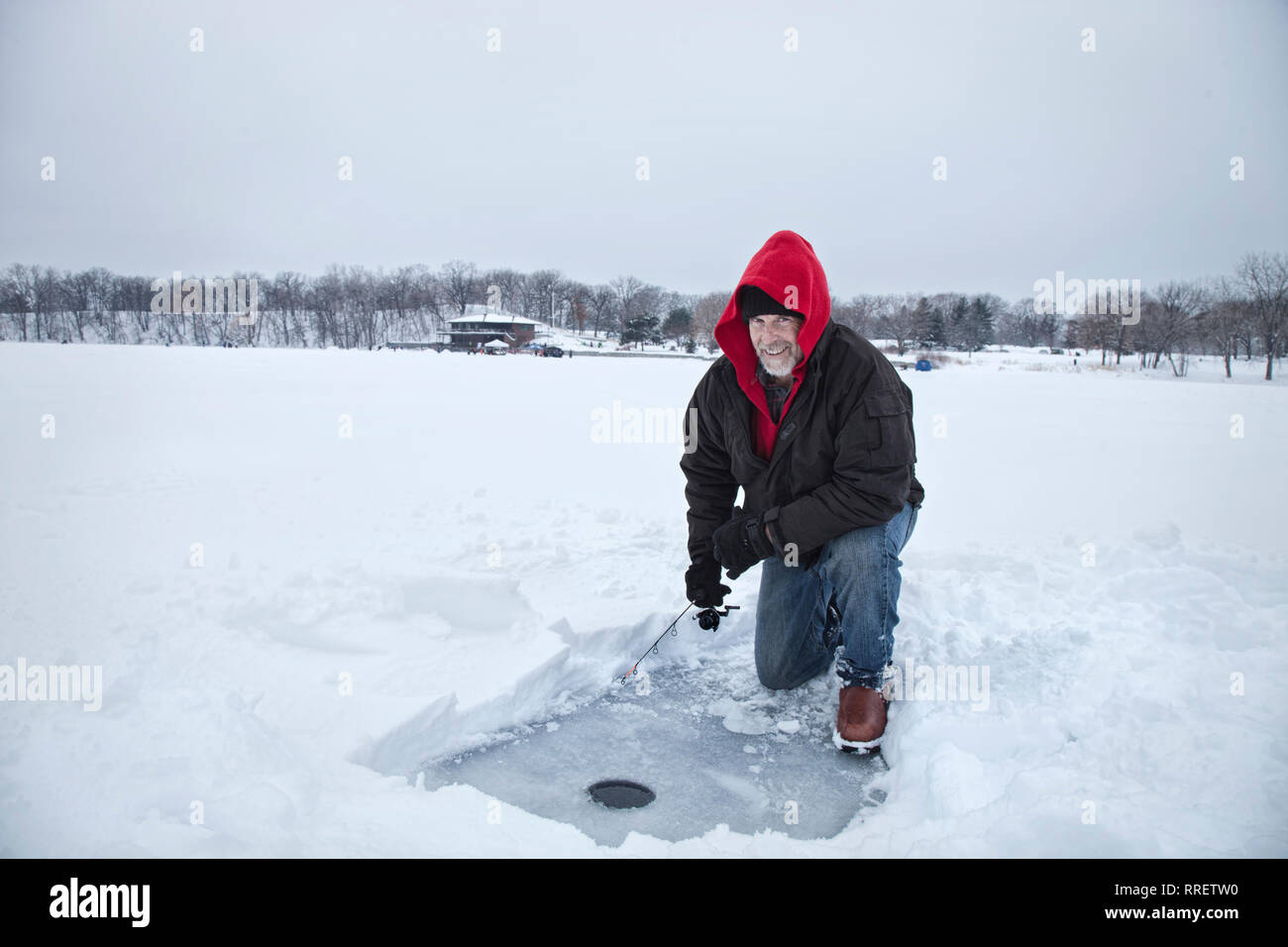 Ein lächelnder Mann mittleren Alters Eisfischen auf einem verschneiten See in Minnesota im Winter Stockfoto