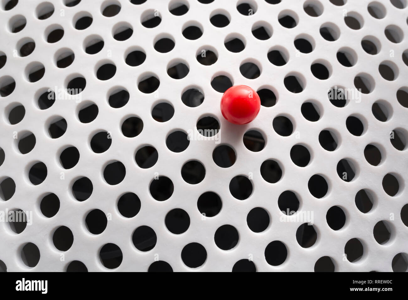 Abstrakte Löcher. Kleine einsame rote Kunststoffkugel isoliert auf runden löchigen weißen Gitter. Angst vor Löchern - trypophobie - Metapher. Auch allein in der Welt. Stockfoto