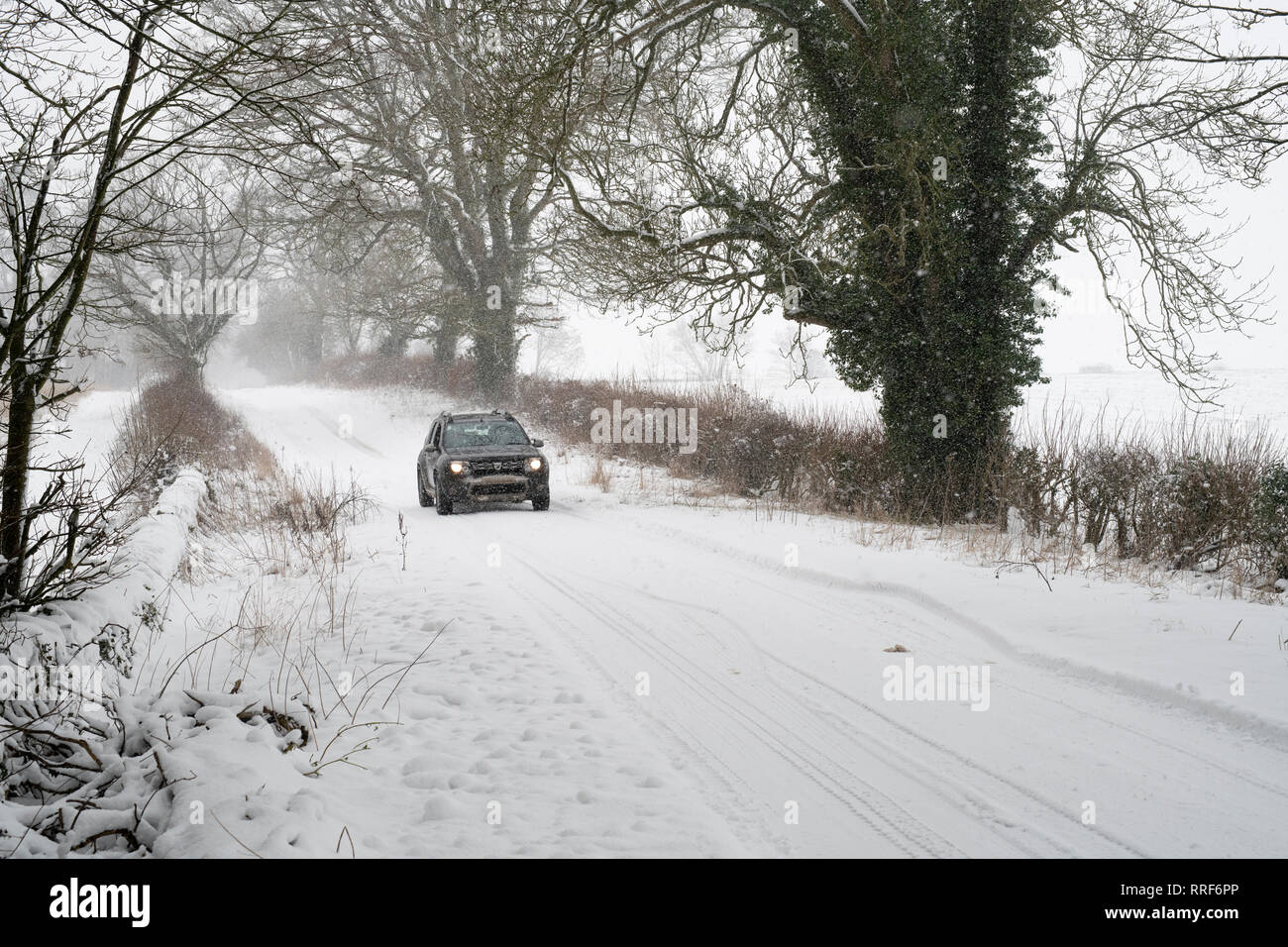 Der Dacia Duster Fahrt auf einer verschneiten Landstraße nahe Eastleach. Cotswolds, Gloucestershire, England Stockfoto