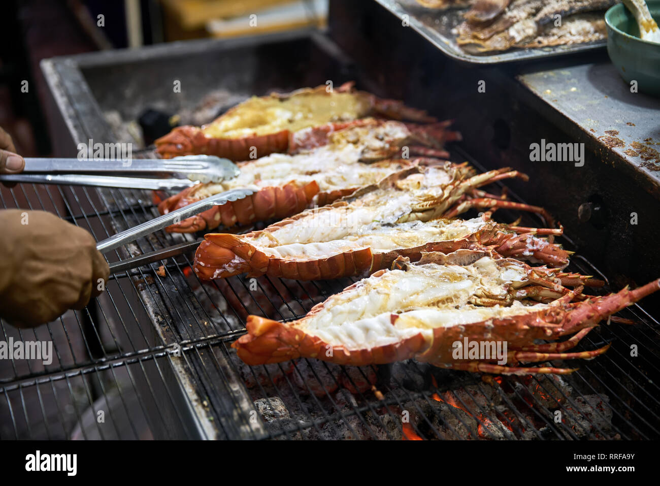 Der Mensch ist das Kochen Hummer auf dem Grill auf der Street Food Market in Bangkok in Thailand. Er Mit chrome Zangen. Closeup horizontale Foto. Stockfoto