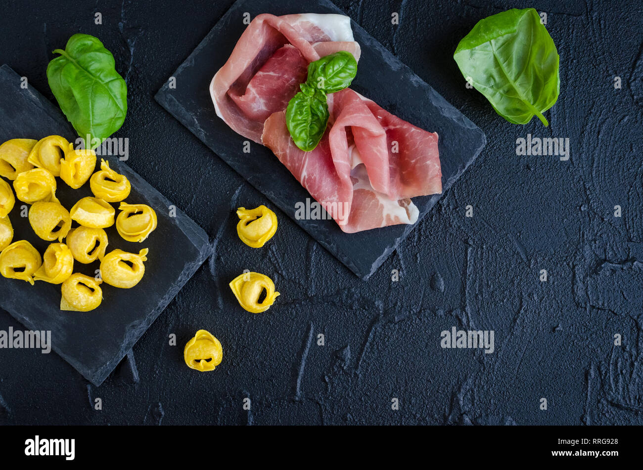 Frisch zubereitete, hausgemachte Fleisch roh Schinken gefüllte Tortellini bereit, auf dunklen Stein Platte mit basilikumblätter auf schwarzem Hintergrund zu kochen. Traditionell I Stockfoto
