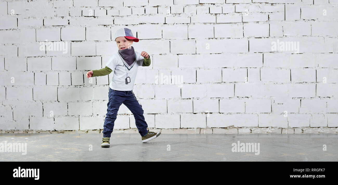 Kind Modell in den jungen Rapper Kleidung posieren. Cool kid Boy dancing Break Dance. Hip-hop Stil. studio, ziegelwand Hintergrund. Banner, kopieren. Stockfoto