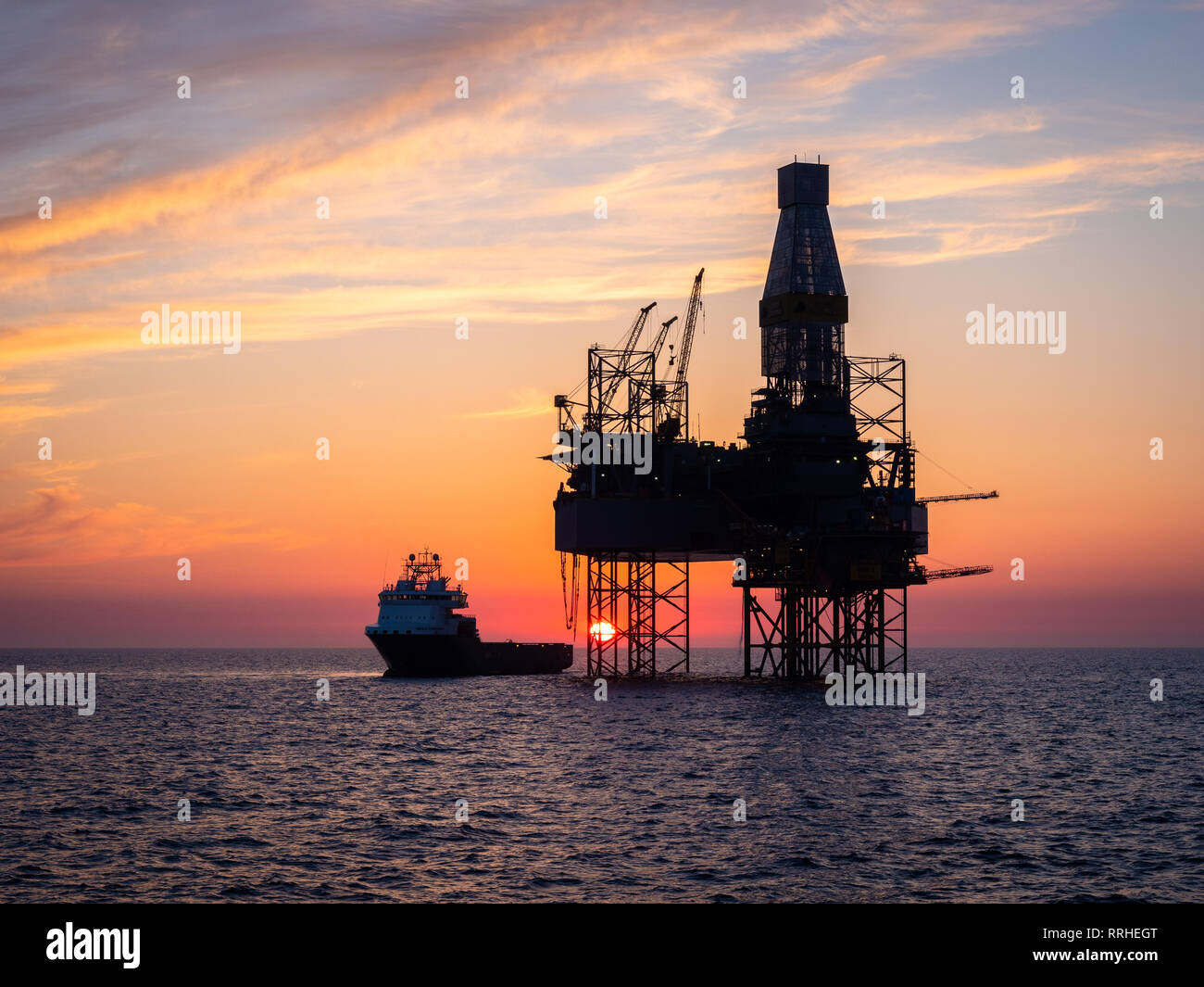 Eine Ölplattform in der Nordsee mit einem Versorgungsschiff neben während des Sonnenuntergangs. Stockfoto