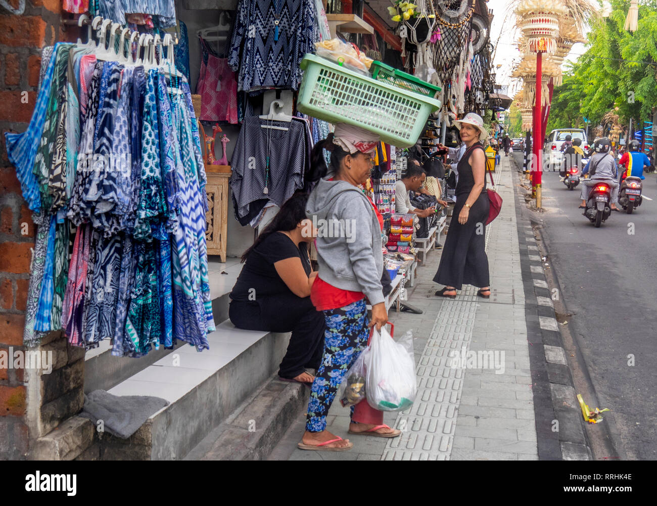 Frau Kopf trägt einen Korb und Kaukasische weibliche Touristen mit roten Tasche auf Jl Raya Legian, Kuta Bali Indonesien. Stockfoto