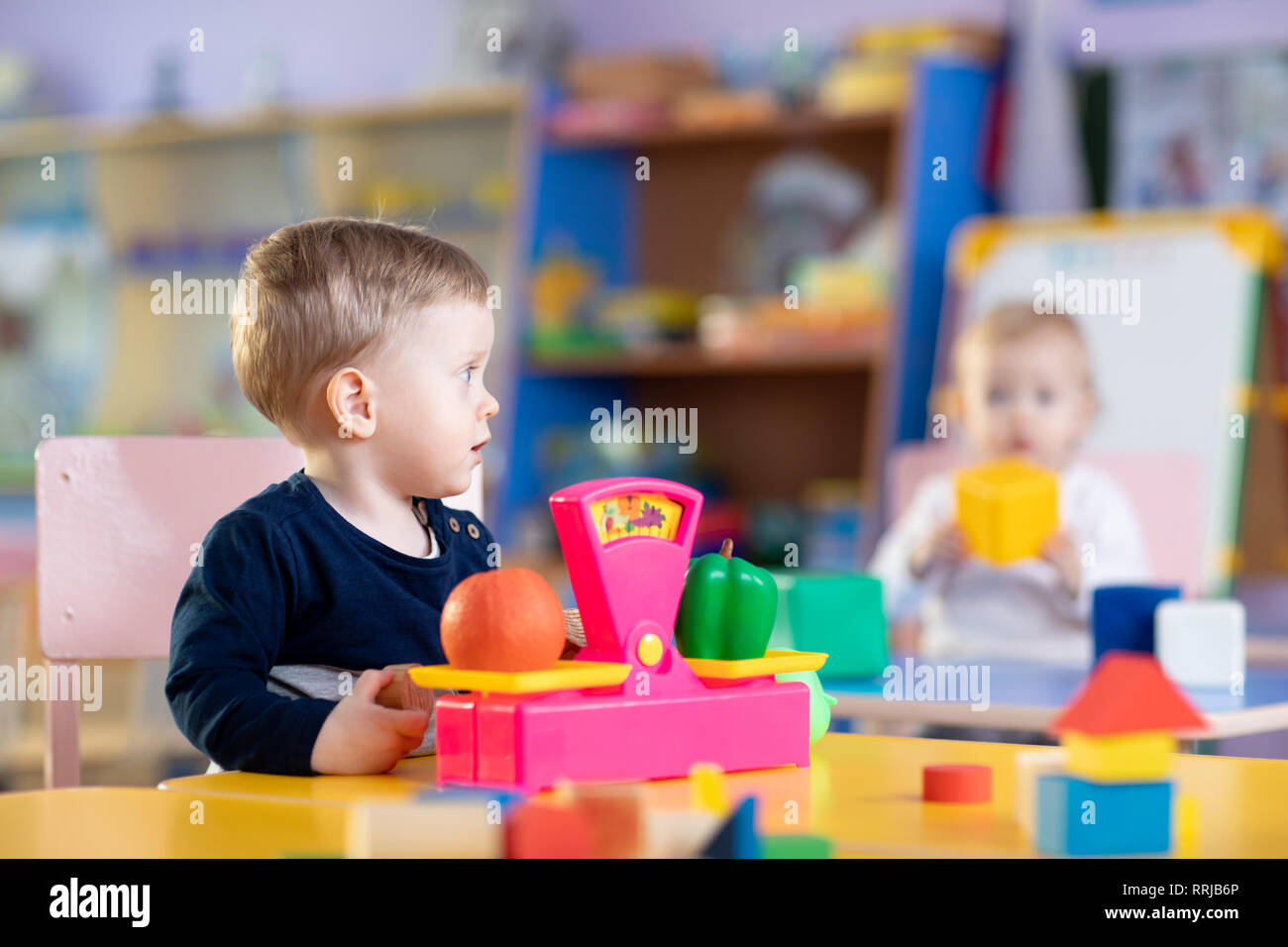 Wenig Kindergarten Kind Junge sitzt am Tisch und spielt mit Spielzeug Waagen im Spielzimmer Stockfoto