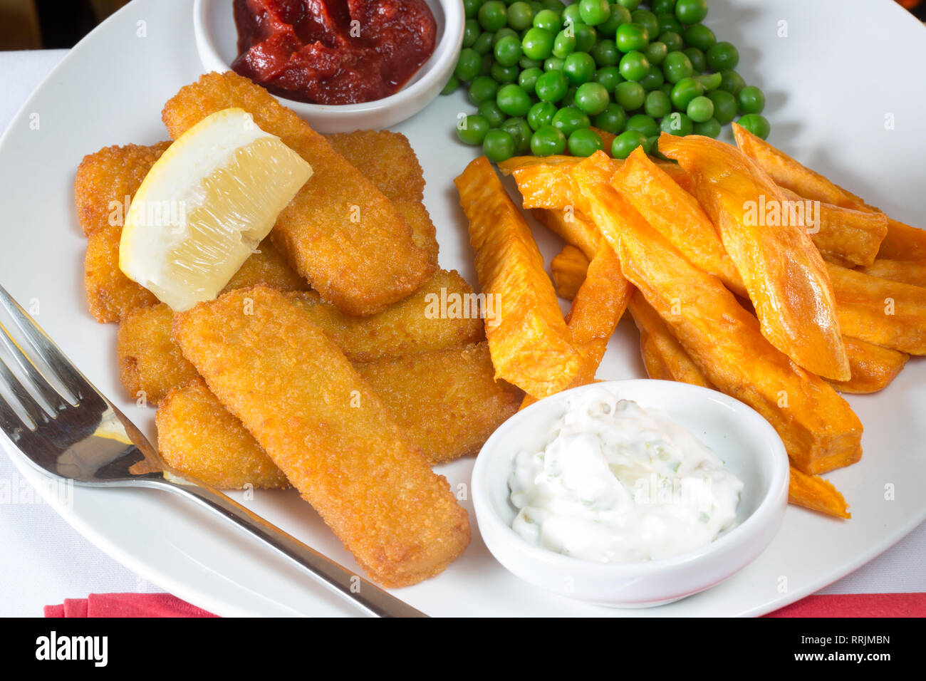 Klassische englische Pub Mittagessen von Fischstäbchen, Pommes und Garten Erbsen serviert mit hausgemachtem Tomatenketchup, Remoulade und frische Zitrone Keil. Stockfoto