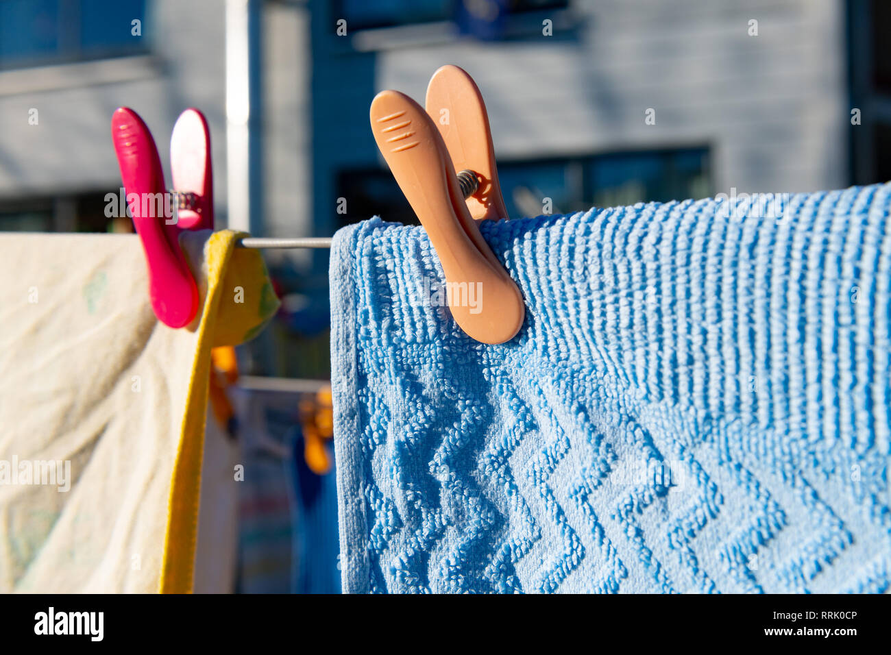 Orange Wäscheklammer hält blau Handtuch auf der Wäscheleine im Hinterhof. Stockfoto
