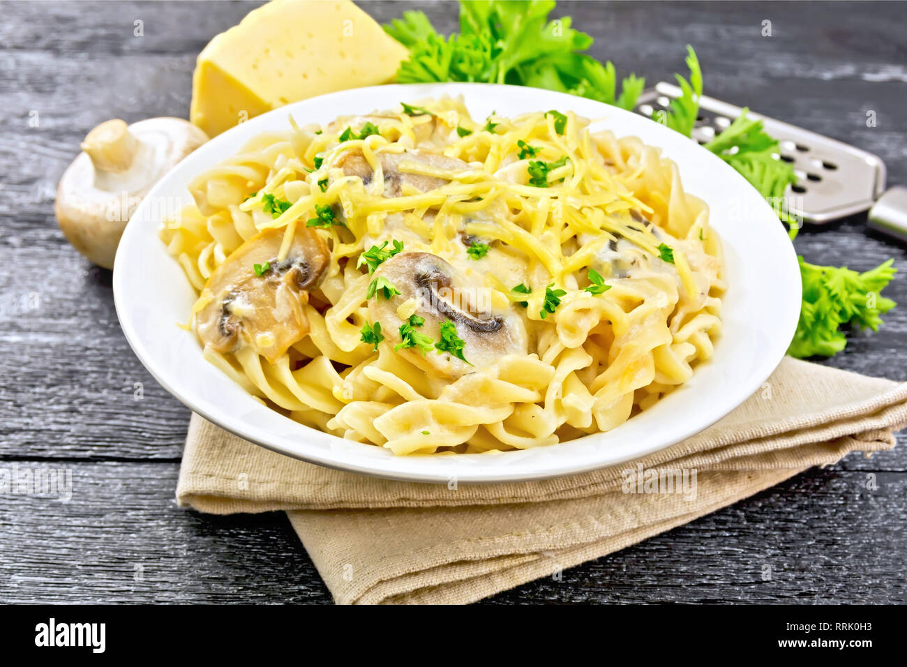 Fusilli mit Champignons in Rahmsauce, Petersilie und geriebenem Käse in einer Platte auf Serviette auf Holzbrett Hintergrund Stockfoto