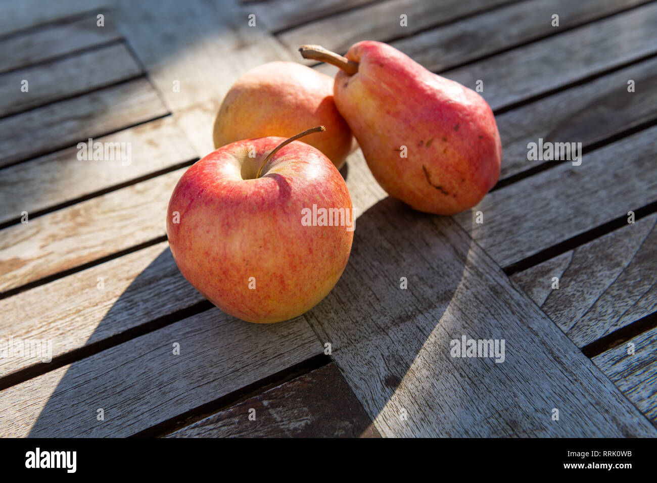 Zwei rote und gelbe Birnen und ein Apple liegen auf einem rustikalen Garten Tisch in der Sonne. Stockfoto