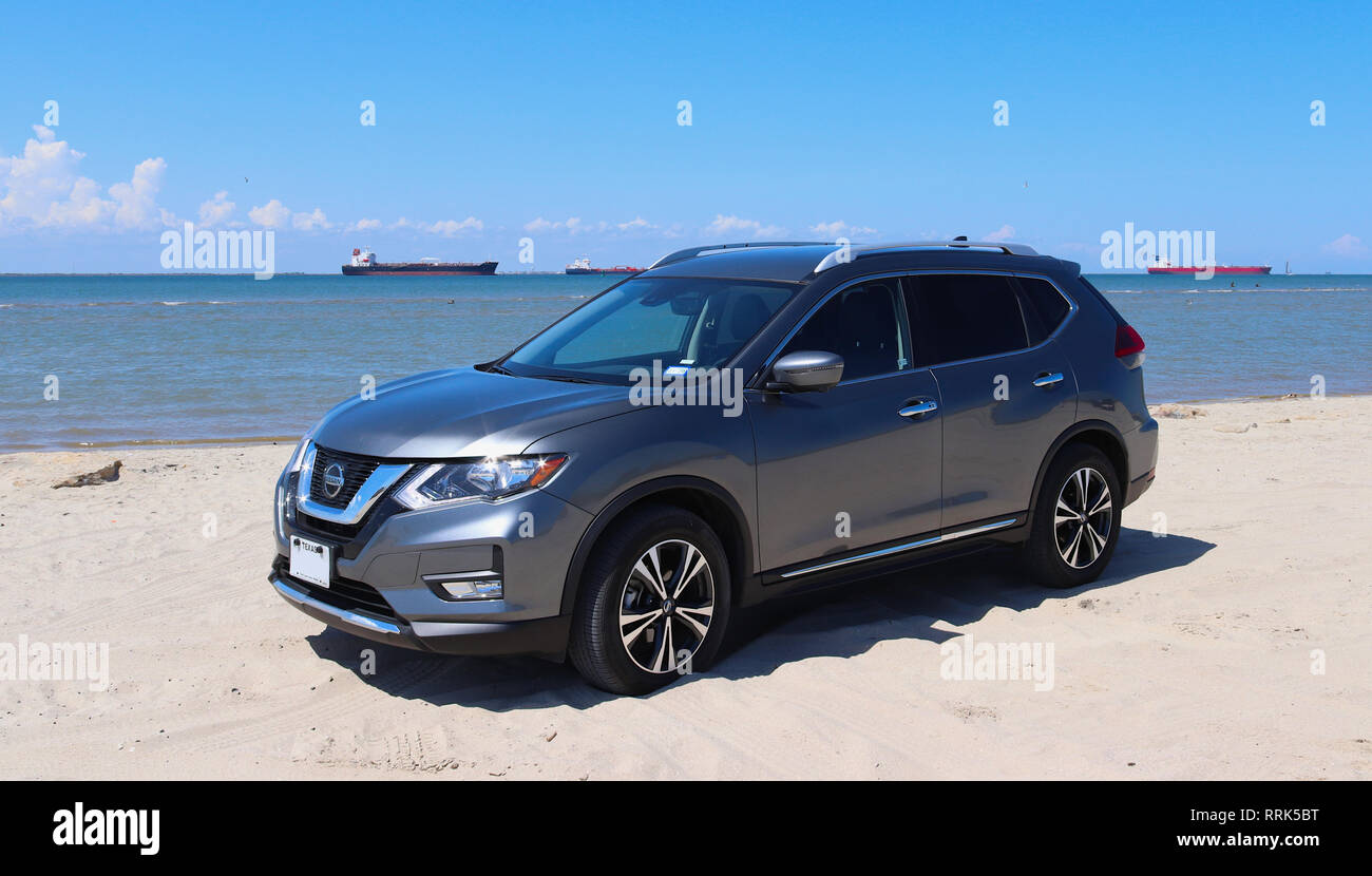 GALVESTON, Texas, USA - Juni 8, 2018: Ein anthrazit Nissan Rogue kompakten Crossover-SUV Auto ist am Strand geparkt. Frachtschiffe navigieren im Golf. Stockfoto