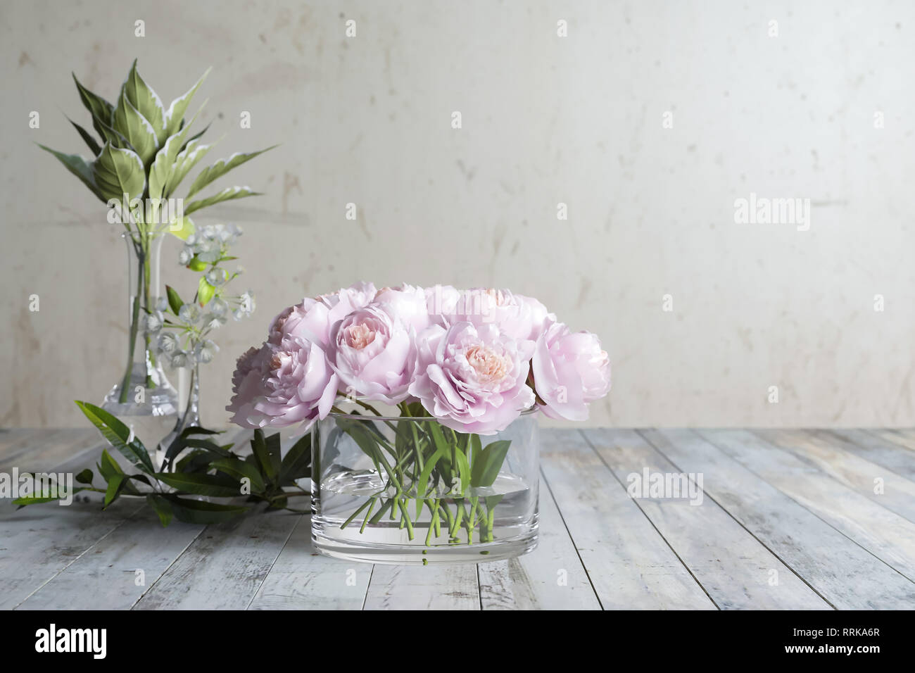 Blumen, Blumen mit Blättern und einem blühenden Zweig stehen auf alten hölzernen Brettern gegen eine einzelne Wand, Glaswaren Stockfoto