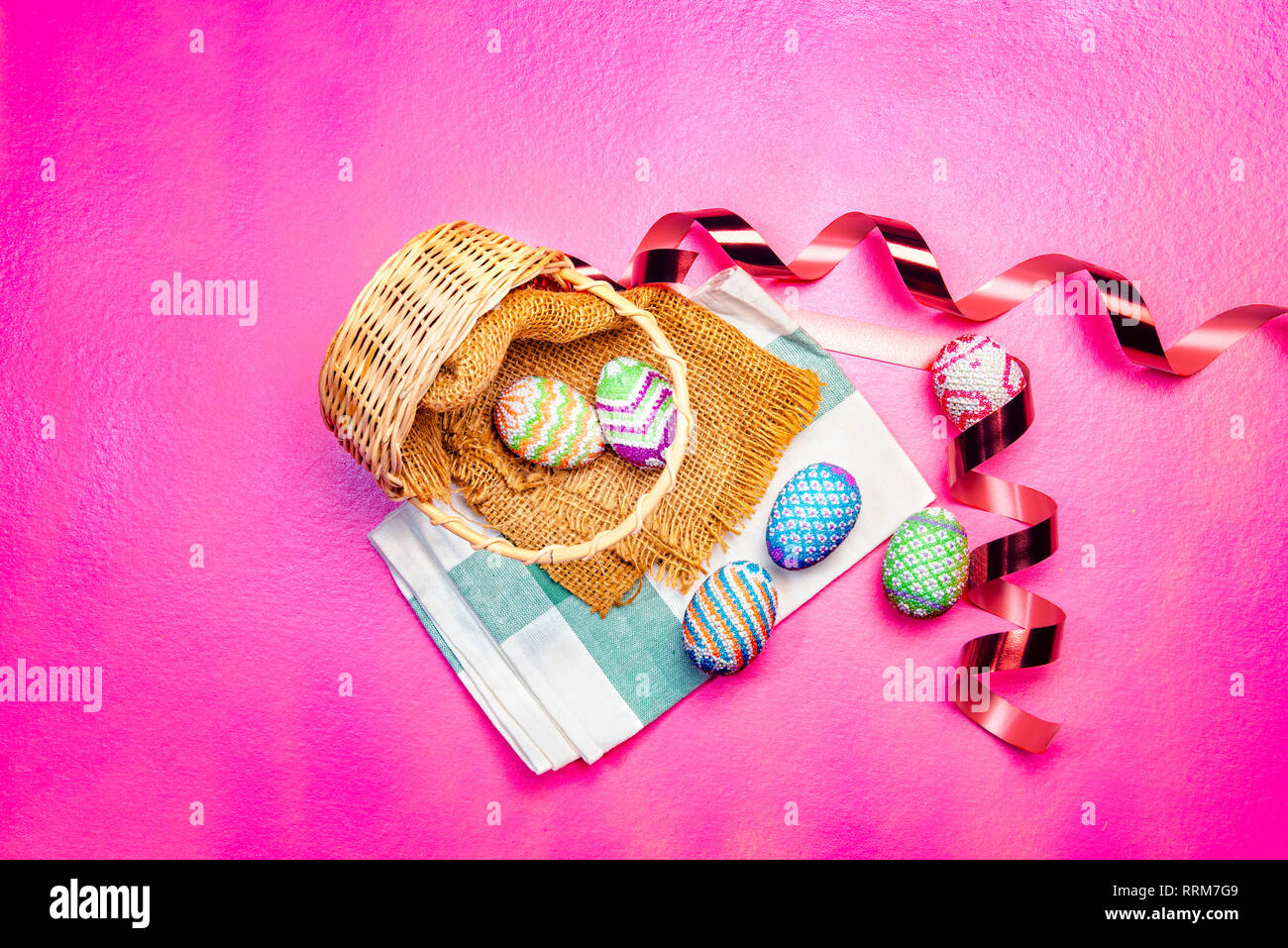 Bunte Ostereier aus Stoff auf Holz- korb mit Serviette und red ribbon über rosa Farbe Hintergrund verschüttet. Frohe Ostern Stockfoto