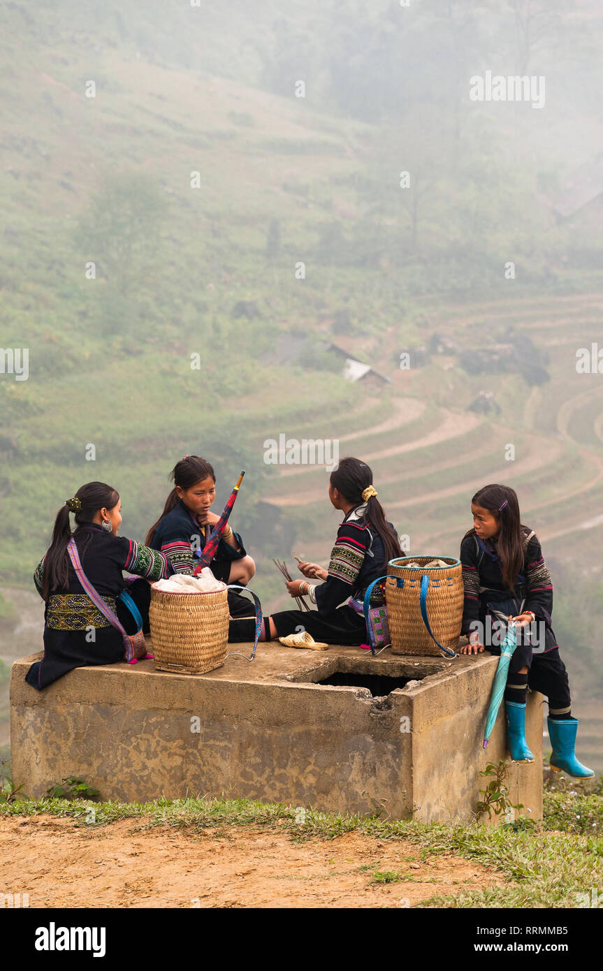 Lokale Hmong Frauen in traditioneller Kleidung sitzen im Gespräch mit terrassierten Feldern im Hintergrund an einem nebligen Tag, Sa Pa, Vietnam Stockfoto