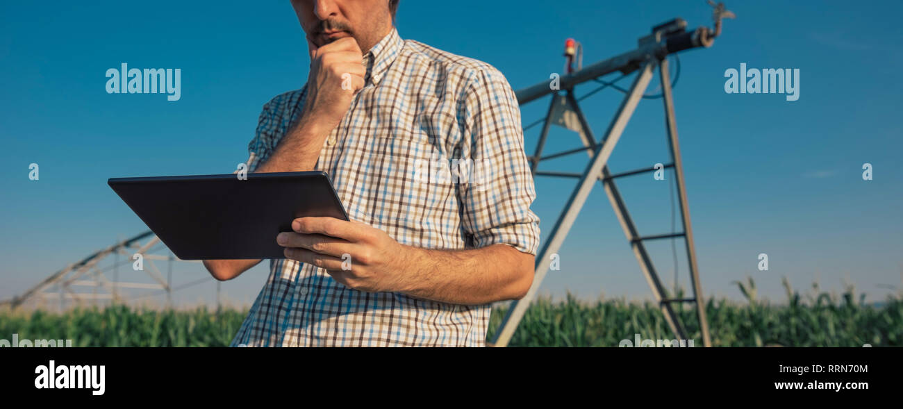Ernsthafte betroffenen Landwirt mit Tablet Computer im Kornfeld mit Bewässerungsanlage außer Betrieb während der warmen Sommertag Stockfoto