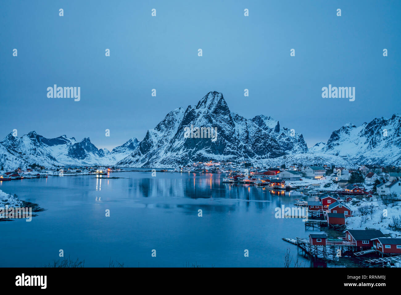 Ruhiger Blick auf verschneite waterfront Fischerdorf und Berge bei Nacht, Reine, Lofoten, Norwegen Stockfoto