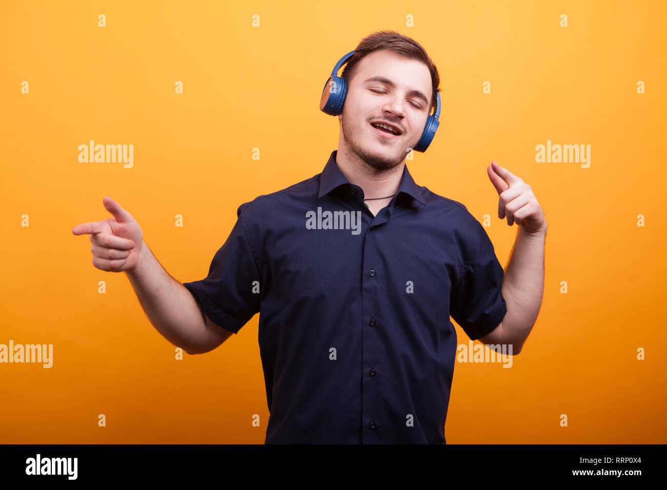 Glückliche junge Mann im blauen T-Shirt Musik hören über Kopfhörer auf gelben Hintergrund. Schöner Mann Stockfoto