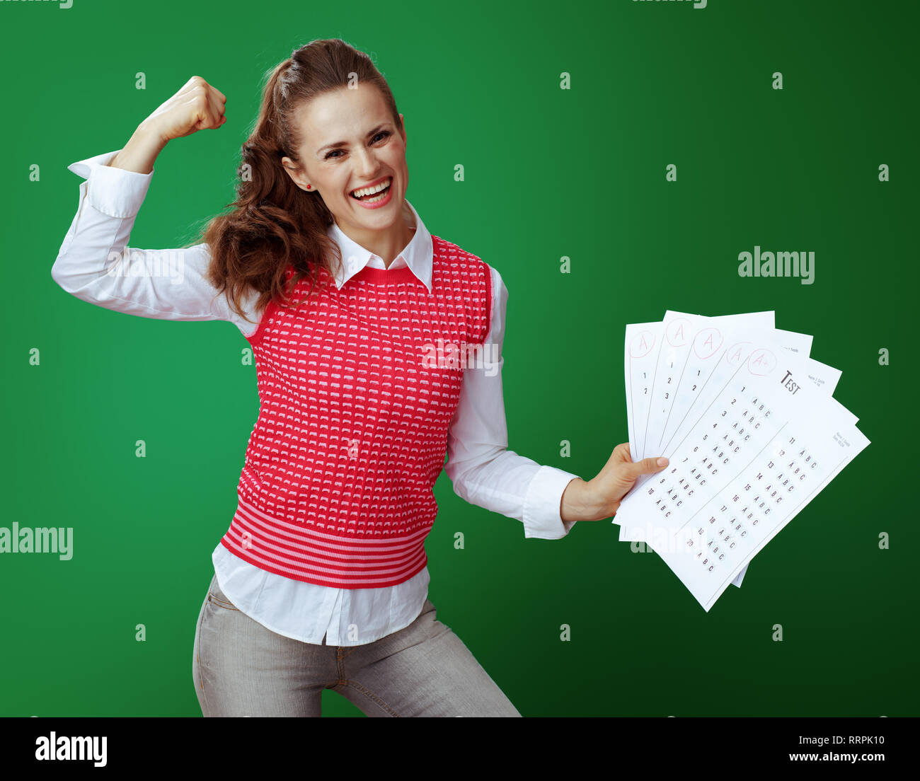 Happy fit Lernende Frau in Grau jeans und Pink ärmelloses Shirt, das einen + Test Ergebnisse und Bizeps auf grünem Hintergrund isoliert. Stockfoto