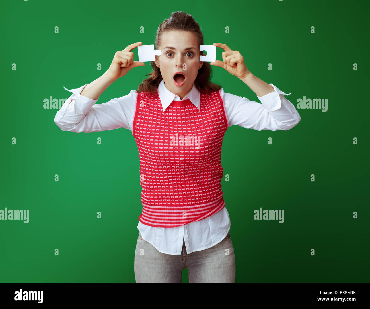 Moderne lerner Frau in Grau jeans und Pink ärmelloses Shirt versuchen, 2 Stück des Puzzles vor grünem Hintergrund zusammenbauen. Analytische th schockiert Stockfoto