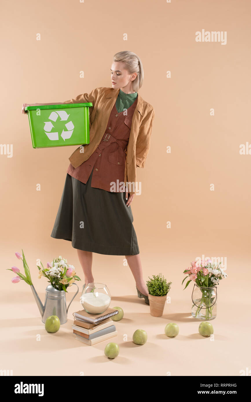 Blonde Frau mit Recycling, in der Nähe von Pflanzen und Blumen auf beigem Hintergrund, Umwelt speichern Konzept Stockfoto