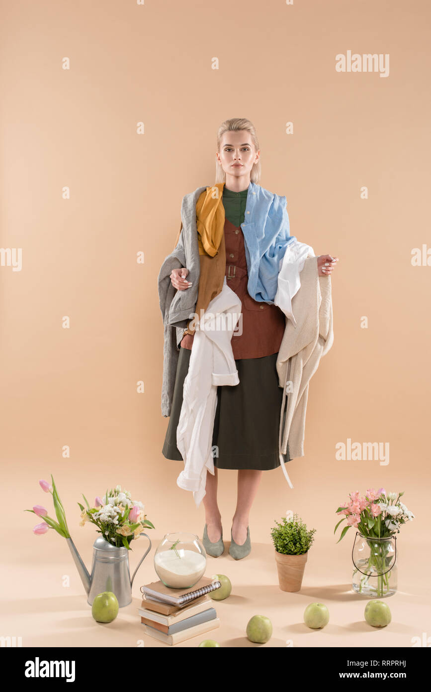 Blonde Frau mit eco Kleidung in der Nähe von Pflanzen und Blumen auf beigem Hintergrund, Umwelt speichern Konzept Stockfoto