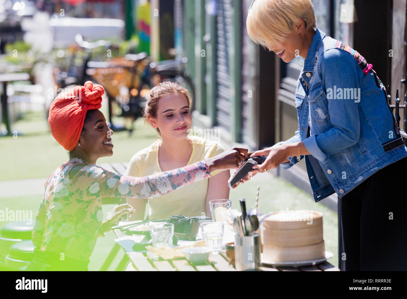 Junge Frau bezahlen Kellnerin mit Kreditkarte an sonnigen Straßencafé Stockfoto