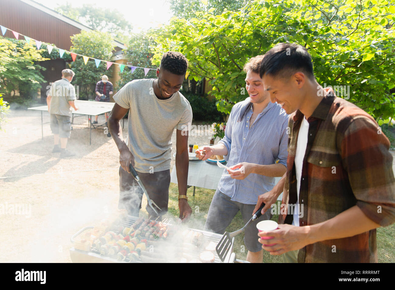 Junge Männer Grillen im sonnigen Hinterhof Stockfoto