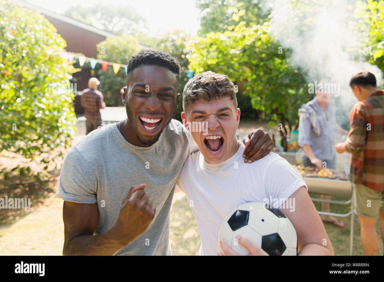 Portrait begeisterte junge Männer, die mit Fußball zujubeln, genießen Garten Grill Stockfoto