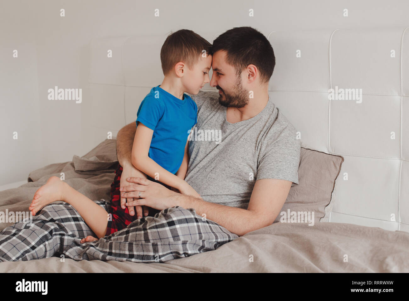 Portrait von mittleren Alter kaukasischen Vater im Gespräch mit jungen Sohn. Mann übergeordneten Holding umarmen mit Kind auf Bett im Schlafzimmer zu Hause. Authentischen Lebensstil Stockfoto