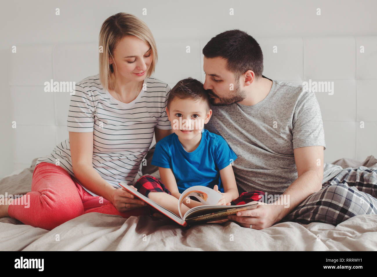 Familie von drei Personen auf dem Bett im Schlafzimmer lesen Buch sitzen.  Mutter, Vater und der Junge Sohn zu Hause Zeit miteinander zu verbringen.  Eltern sprechen, kommunizieren Stockfotografie - Alamy