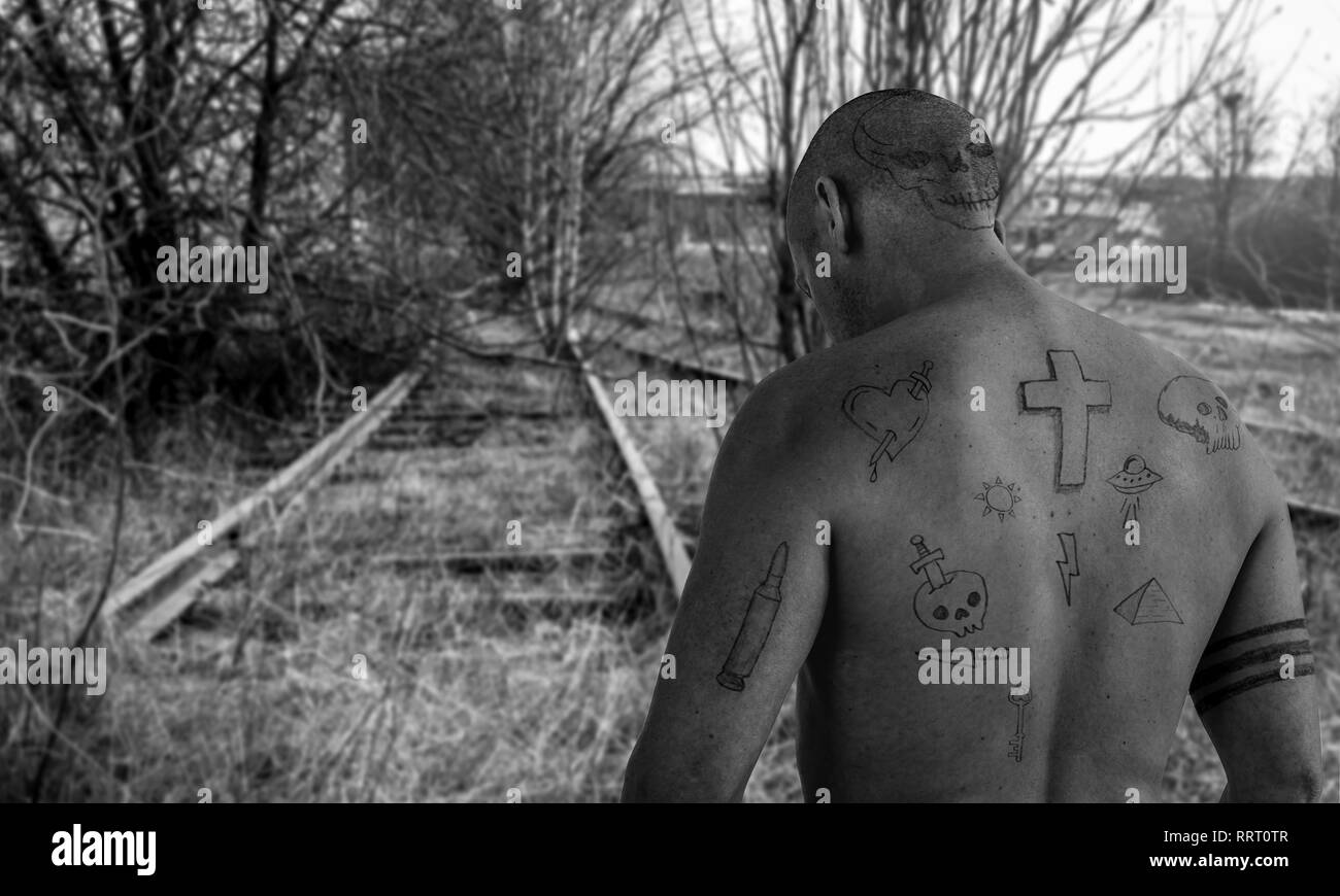 Kerl mit Doodle Tattoos zu Fuß auf verlassenen railroad Track. Kriminelle, überführen Sie entkommen und Gefängnis tattoo Konzept. Bild Montage. Stockfoto