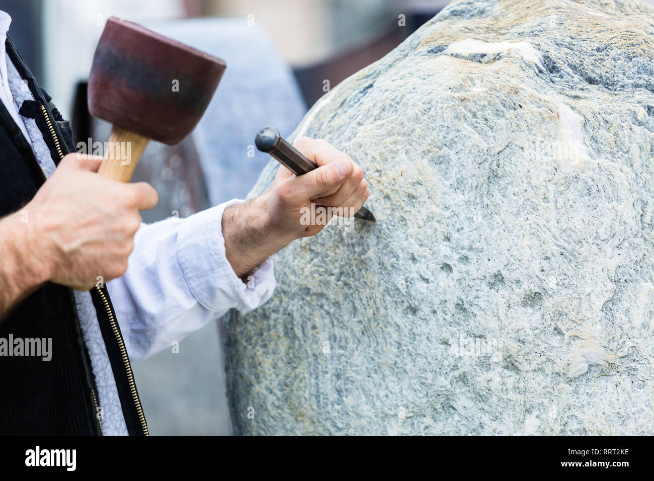 Bildhauer mit Hammer und Cutter arbeiten auf erratischen Block Stockfoto