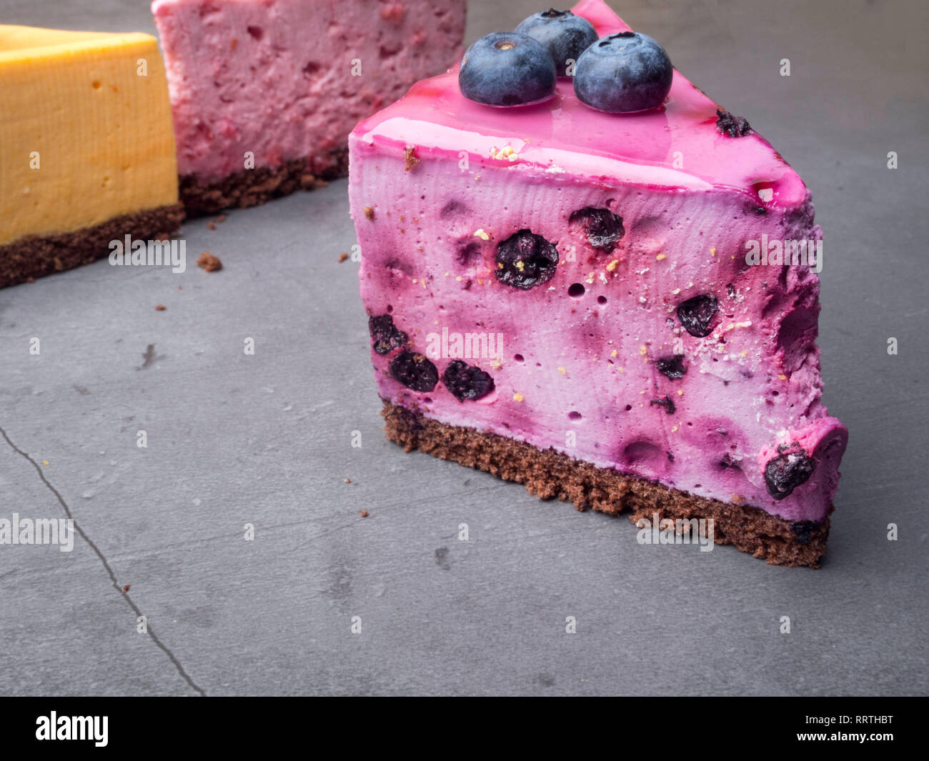 Blueberry cheesecake auf Beton mit Blaubeeren, im Hintergrund gelb und rosa Kuchen, selektiven Fokus Stockfoto