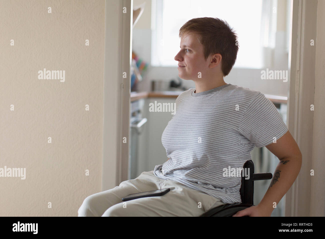 Nachdenkliche junge Frau im Rollstuhl zu Hause Stockfoto