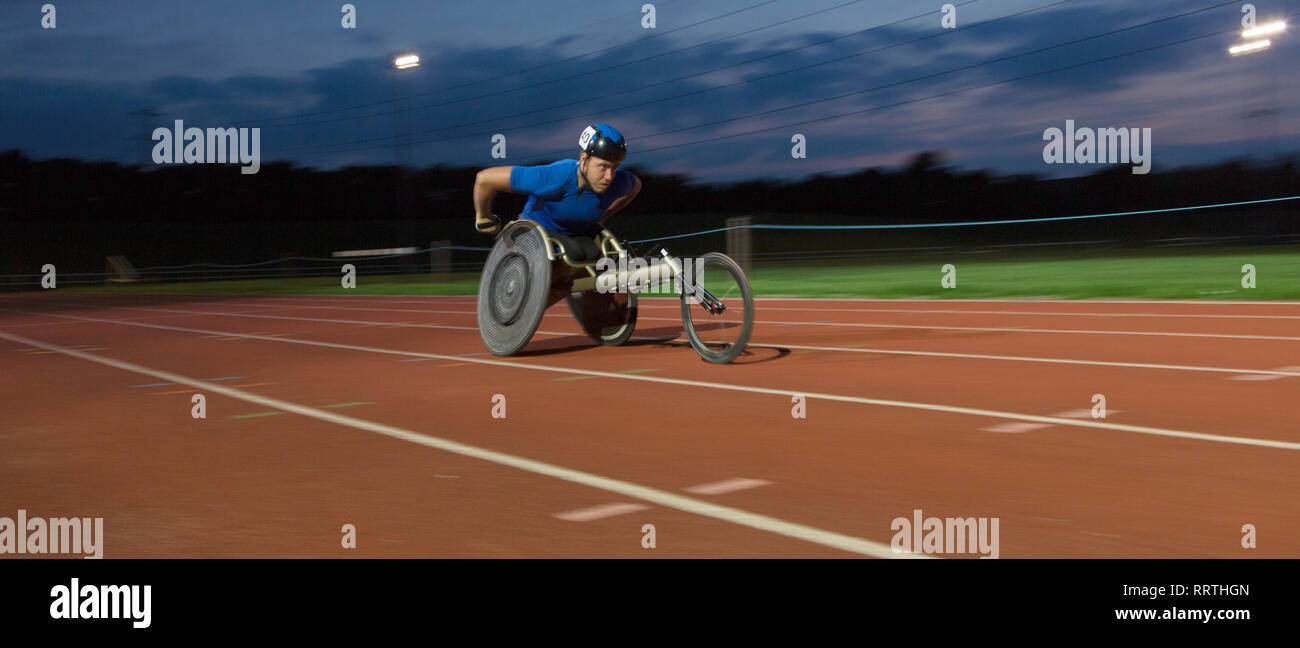 Bestimmt jungen männlichen querschnittsgelähmten Athlet Beschleunigung zusammen Sport Track im Rollstuhl Rennen bei Nacht Stockfoto